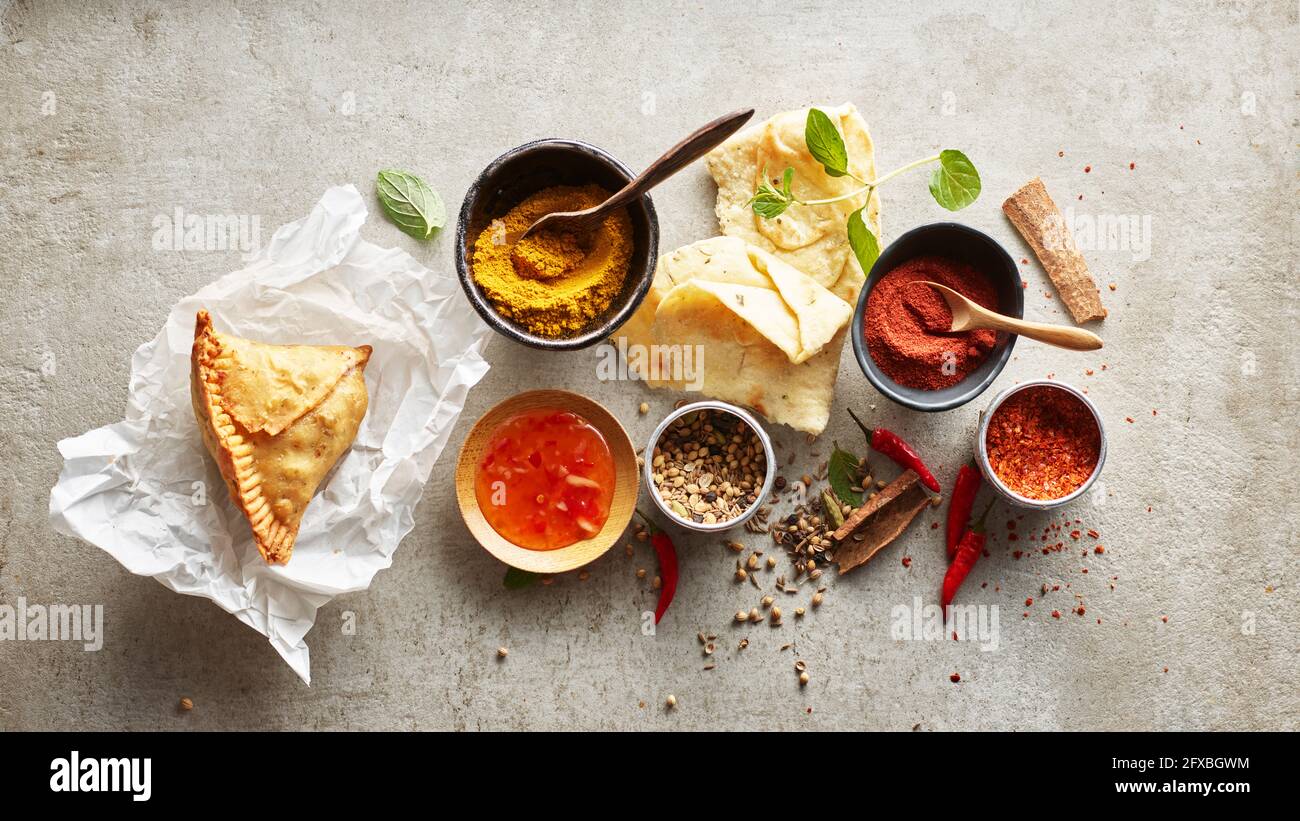 Studioaufnahme von Samosa-Knödel auf Papierservietten, Masala-Gewürzen, Chili-Dipping-Sauce, Naan-Brot und roten Chilischoten Stockfoto