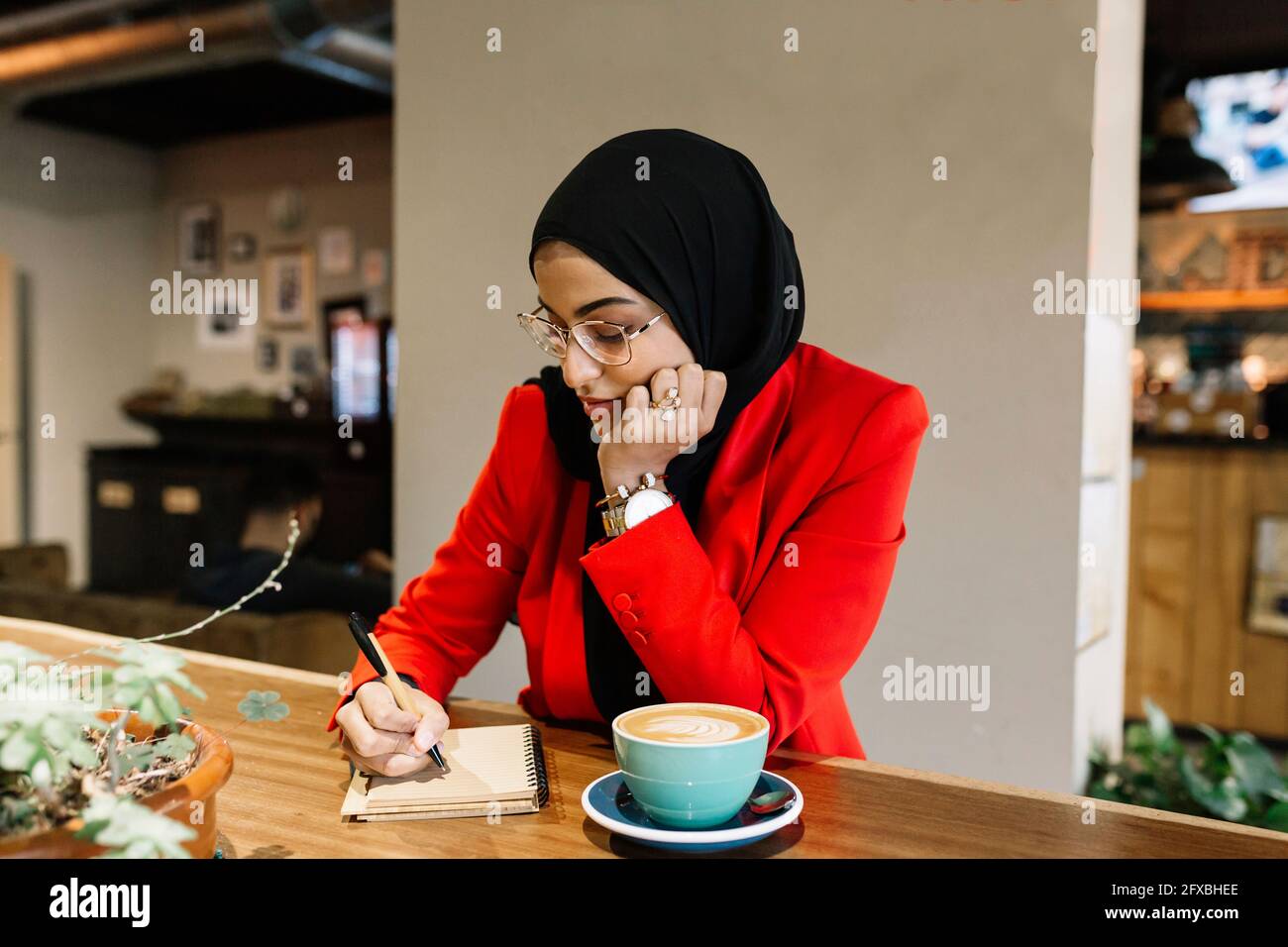 Geschäftsfrau mit Hand auf dem Kinn, die im Café Tagebuch schreibt Stockfoto