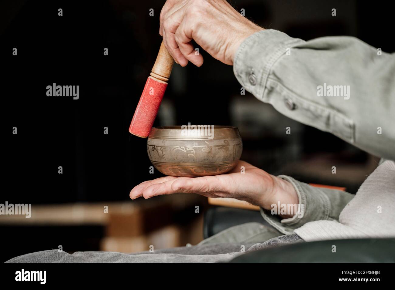 Älterer Mann spielt zu Hause eine tibetische Klangschale Stockfoto