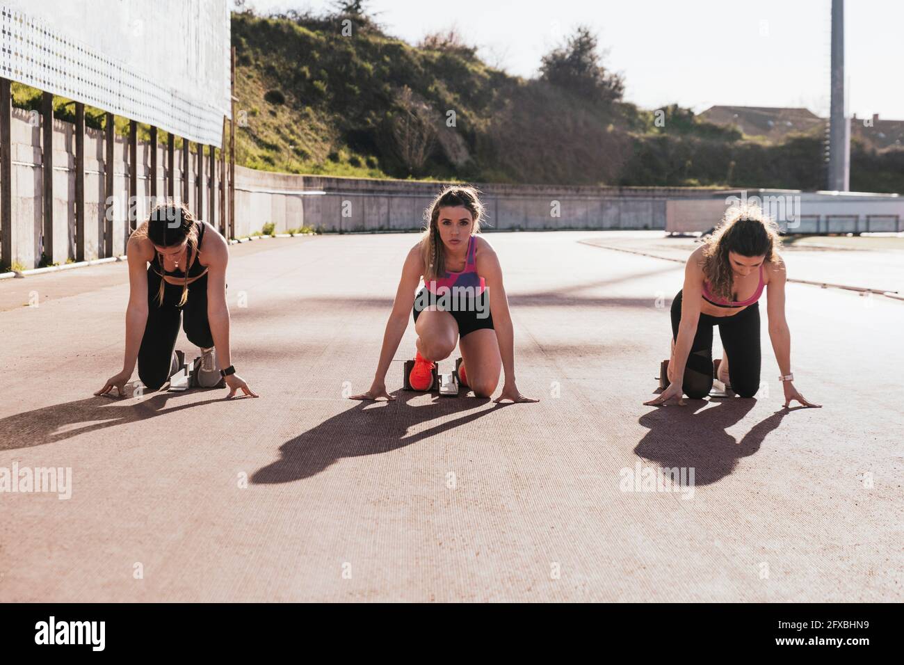 Sportlerinnen knien während der Vorbereitung auf das Rennen an sonnigen Tagen Stockfoto
