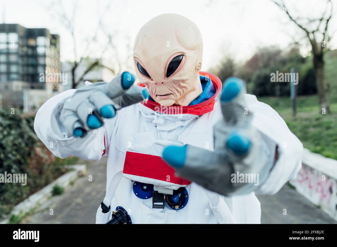 Weibliche Astronautin mit Alien-Maske, die im Freien gestikelt Stockfoto