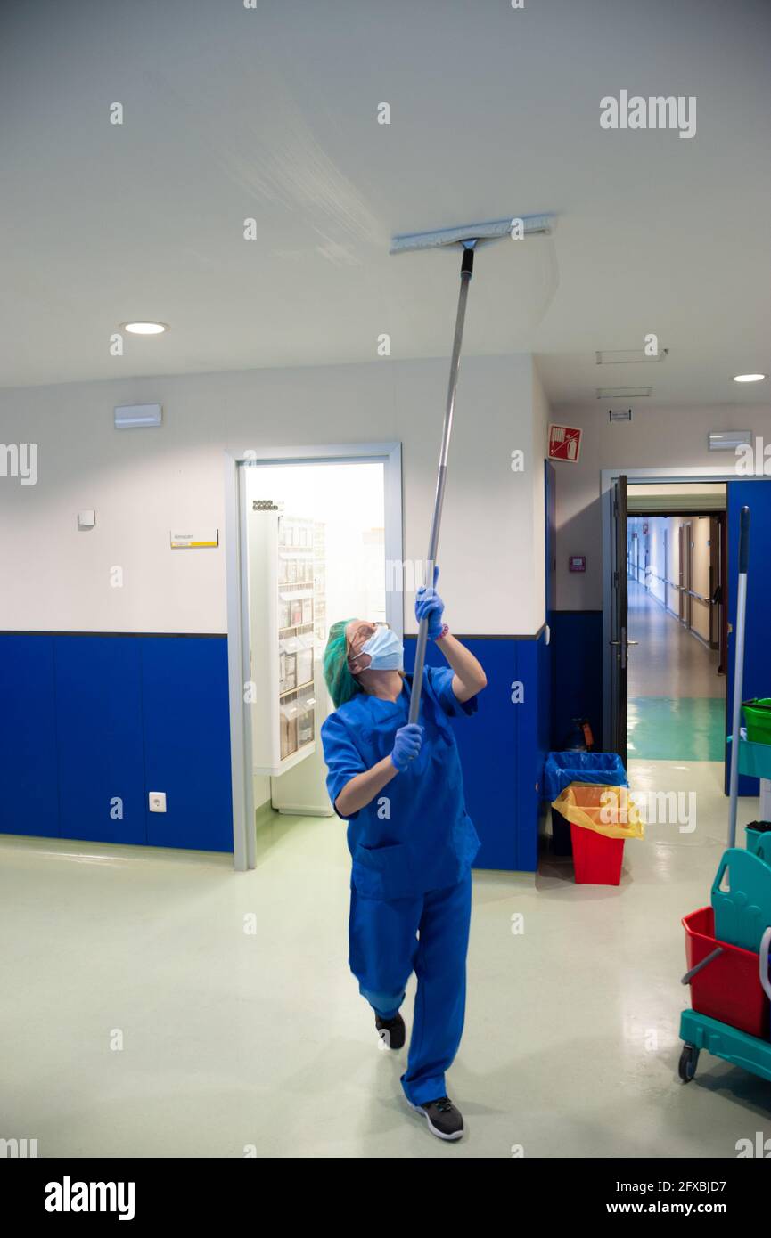 Frau vom Reinigungsservice eines Krankenhauses, die die Decke des Voroperationssaal mit einer speziellen Bürste reinigt. Sanitärkonzept Stockfoto