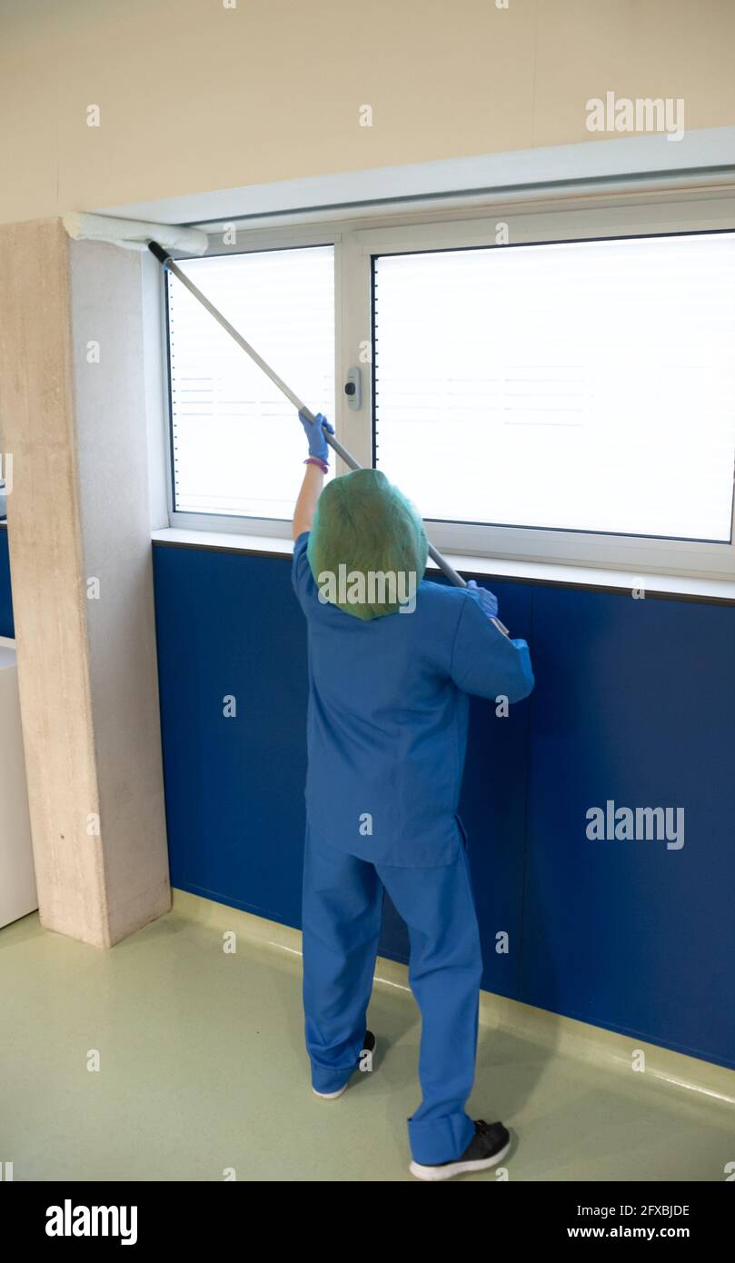 Frau vom Reinigungsservice eines Krankenhauses, die die Fenster des Voroperationsraums mit einer speziellen Bürste reinigt. Sanitärkonzept Stockfoto
