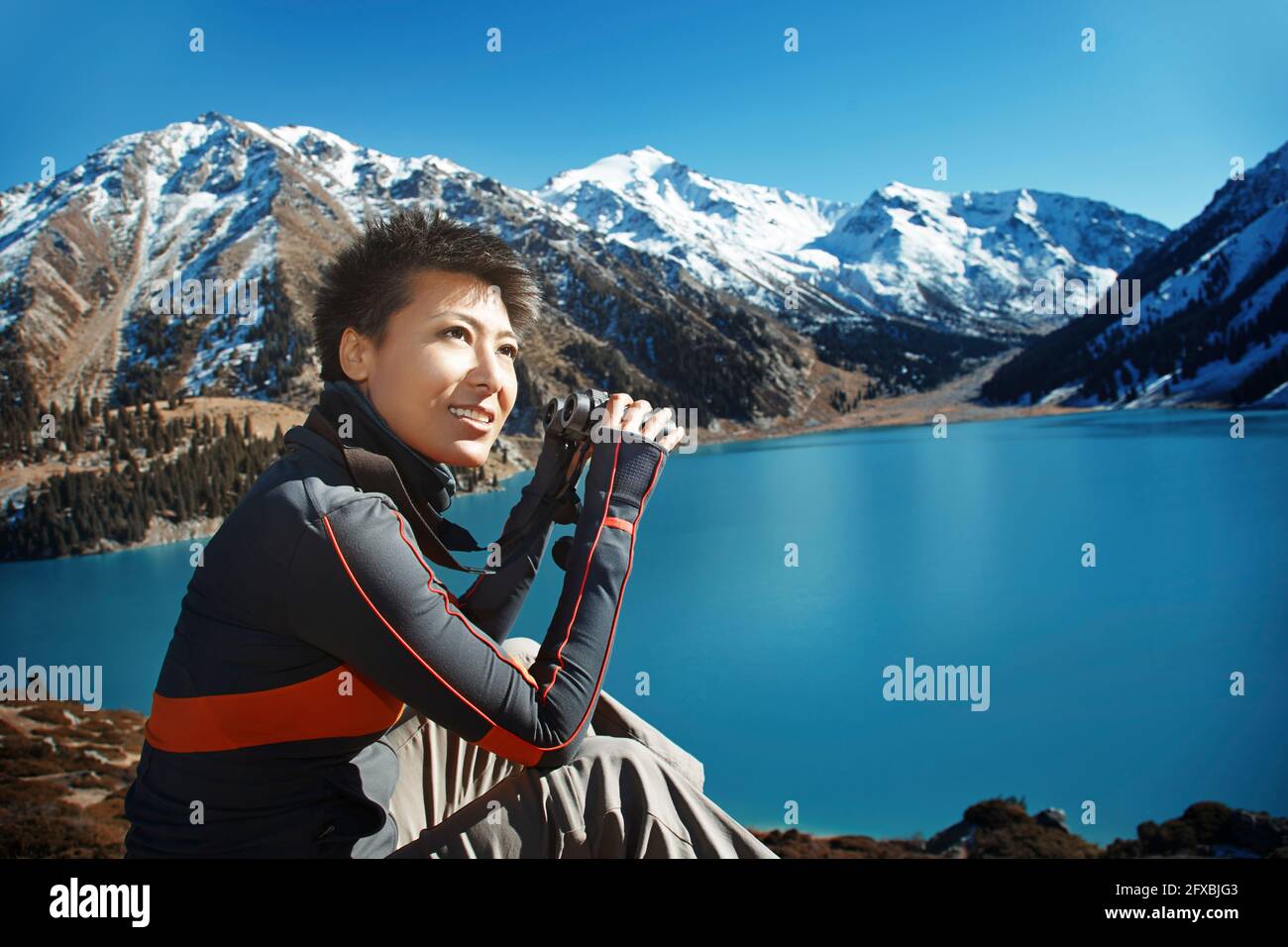 Frau mit kurzen Haaren schaut weg, während sie am See sitzt Stockfoto