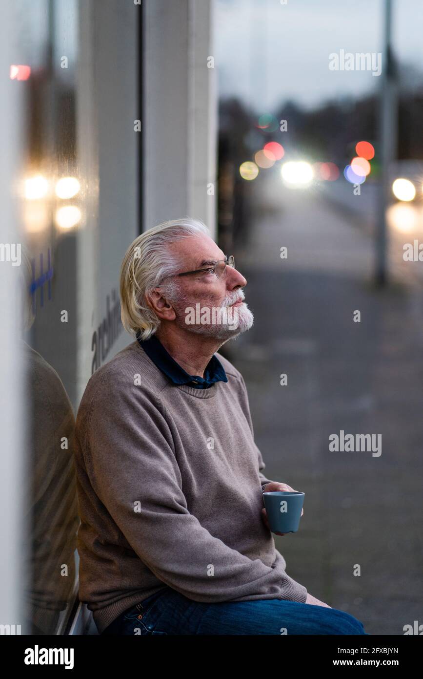 Nachdenklicher älterer Mann, der vor dem Café auf der Straße sitzt Stockfoto