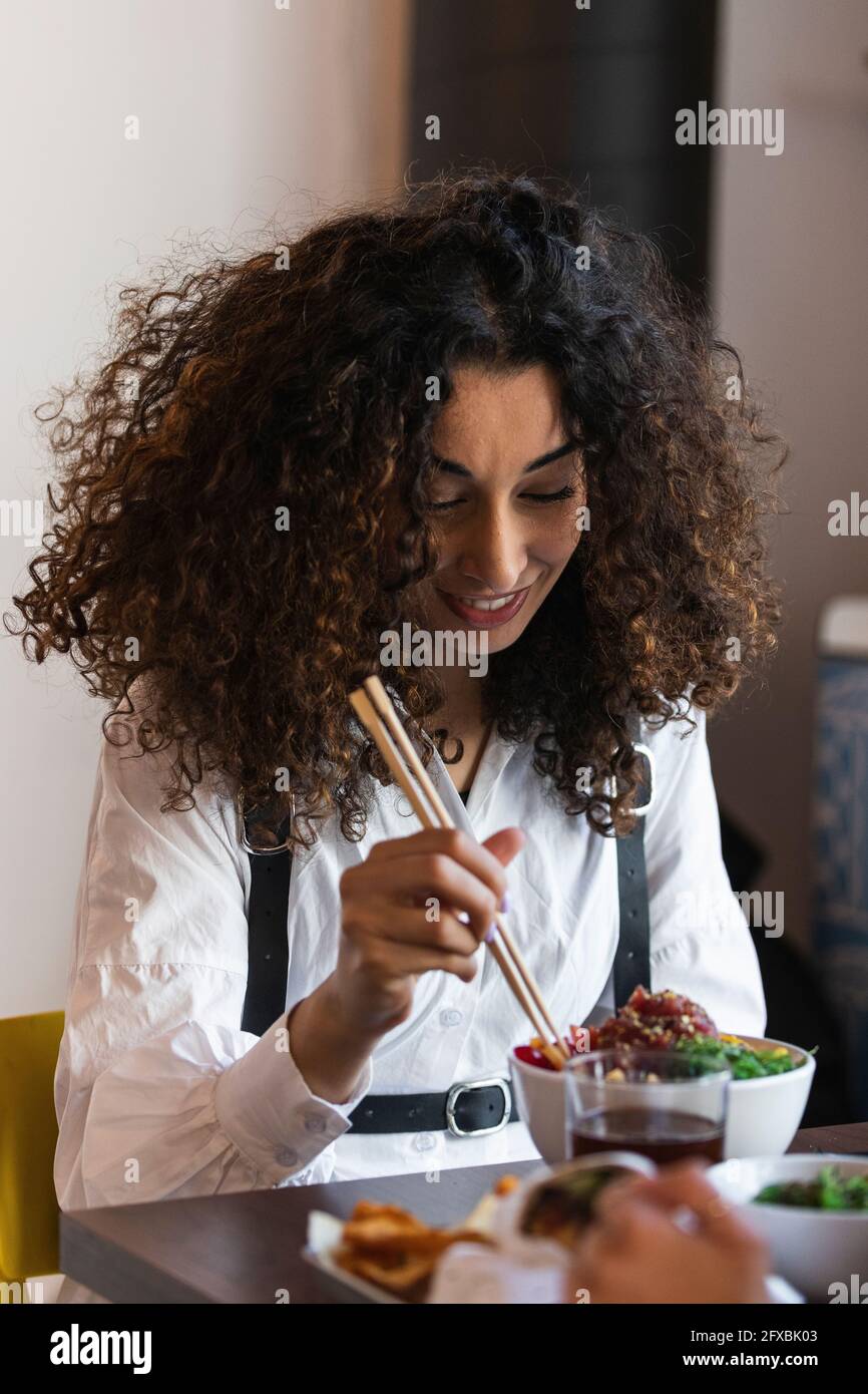 Junge Frau mit lockigen Haaren beim Essen im Restaurant Stockfoto