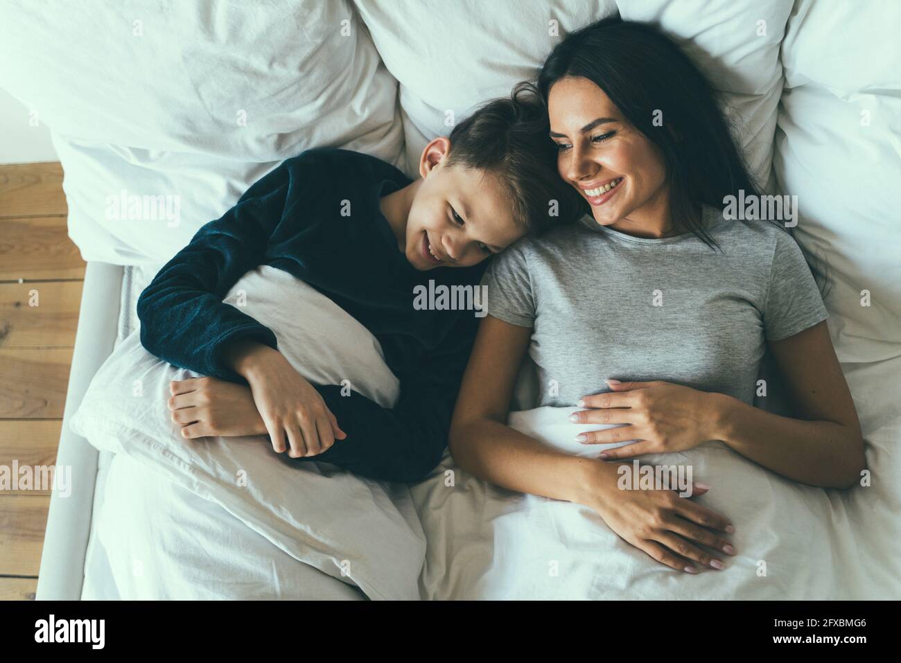 Lächelnder Sohn und Mutter liegen zu Hause auf dem Bett Stockfoto