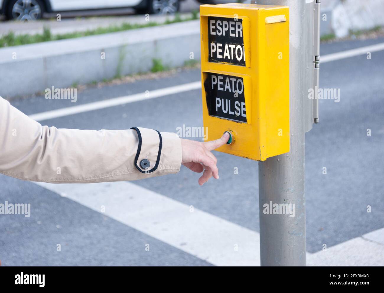 Der Finger einer Frau drückt auf die Fußgängertaste einer Ampel. Die Wörter, die erscheinen, bedeuten: „zu Fuß warten“, „zu Fuß drücken“. Stockfoto