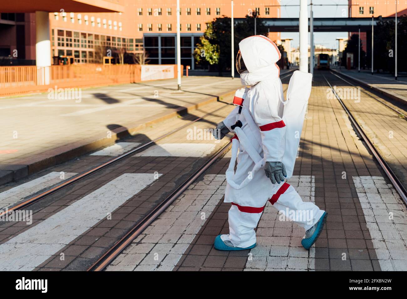 Weibliche Astronautin im Raumanzug, die in der Stadt Straßenbahnlinien überquert Stockfoto