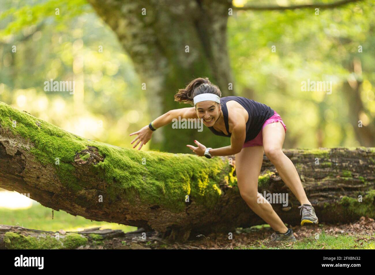 Aktive junge Trailrunnerin, die im Wald über einen gefallenen Baum springt Stockfoto