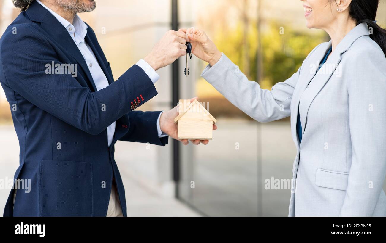 Männlicher Immobilienentwickler mit Architekturmodell, das Geschäftsfrau den Hausschlüssel gibt Stockfoto