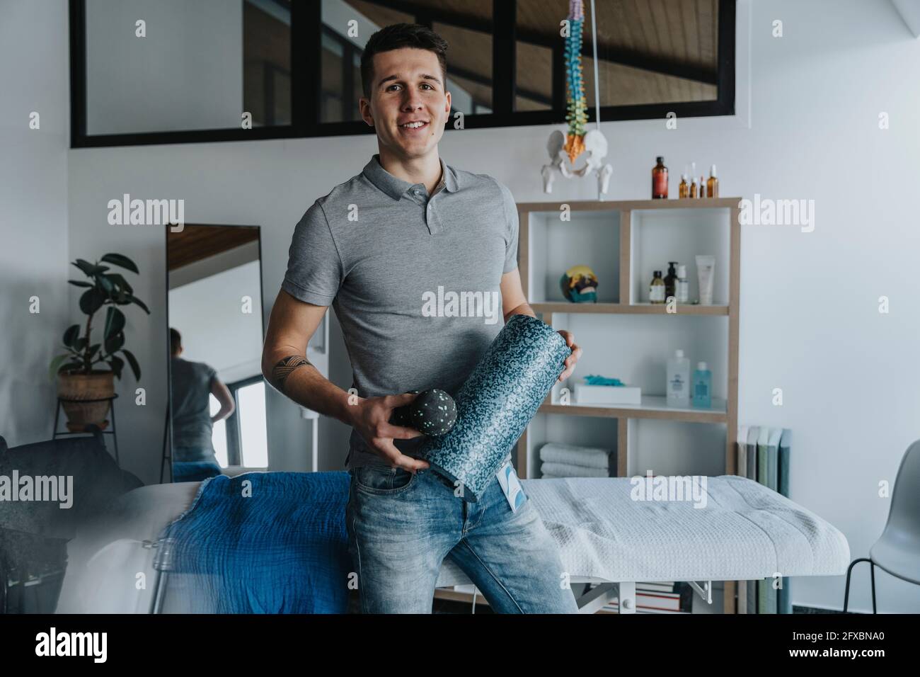 Hübscher männlicher Physiotherapeut, der in der Praxis Schaumstoffrolle hält Stockfoto