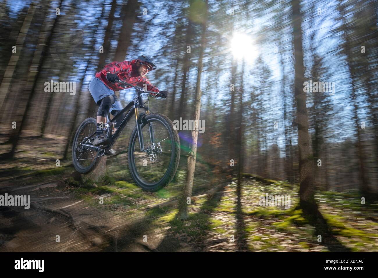 Männlicher Athlet in der Luft mit Mountainbike im Wald Stockfoto