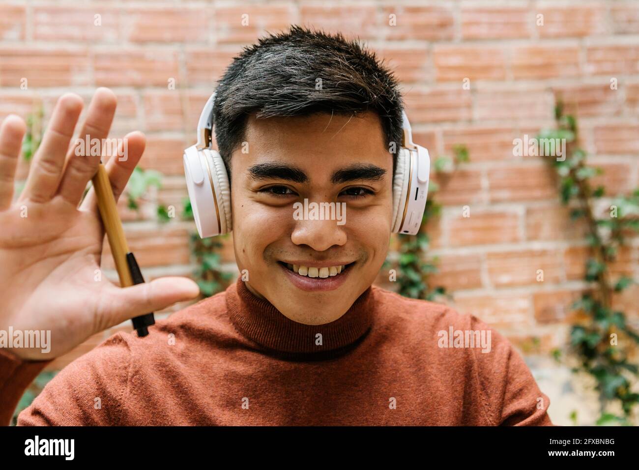 Junger Unternehmer mit Kopfhörern, die Hand in der Cafeteria winken Stockfoto