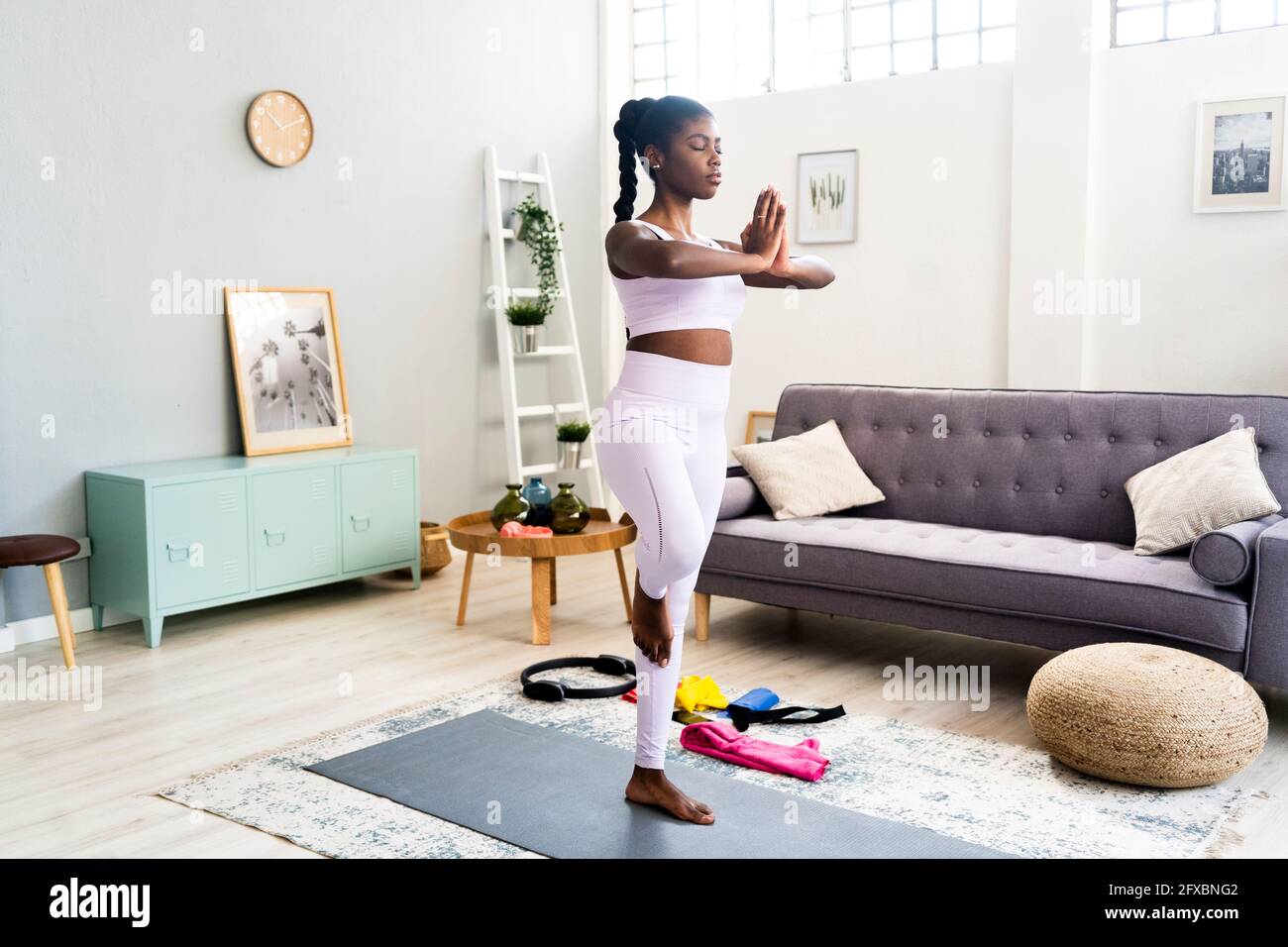 Junge Frau, die auf einem Bein steht, während sie zu Hause Yoga macht Stockfoto