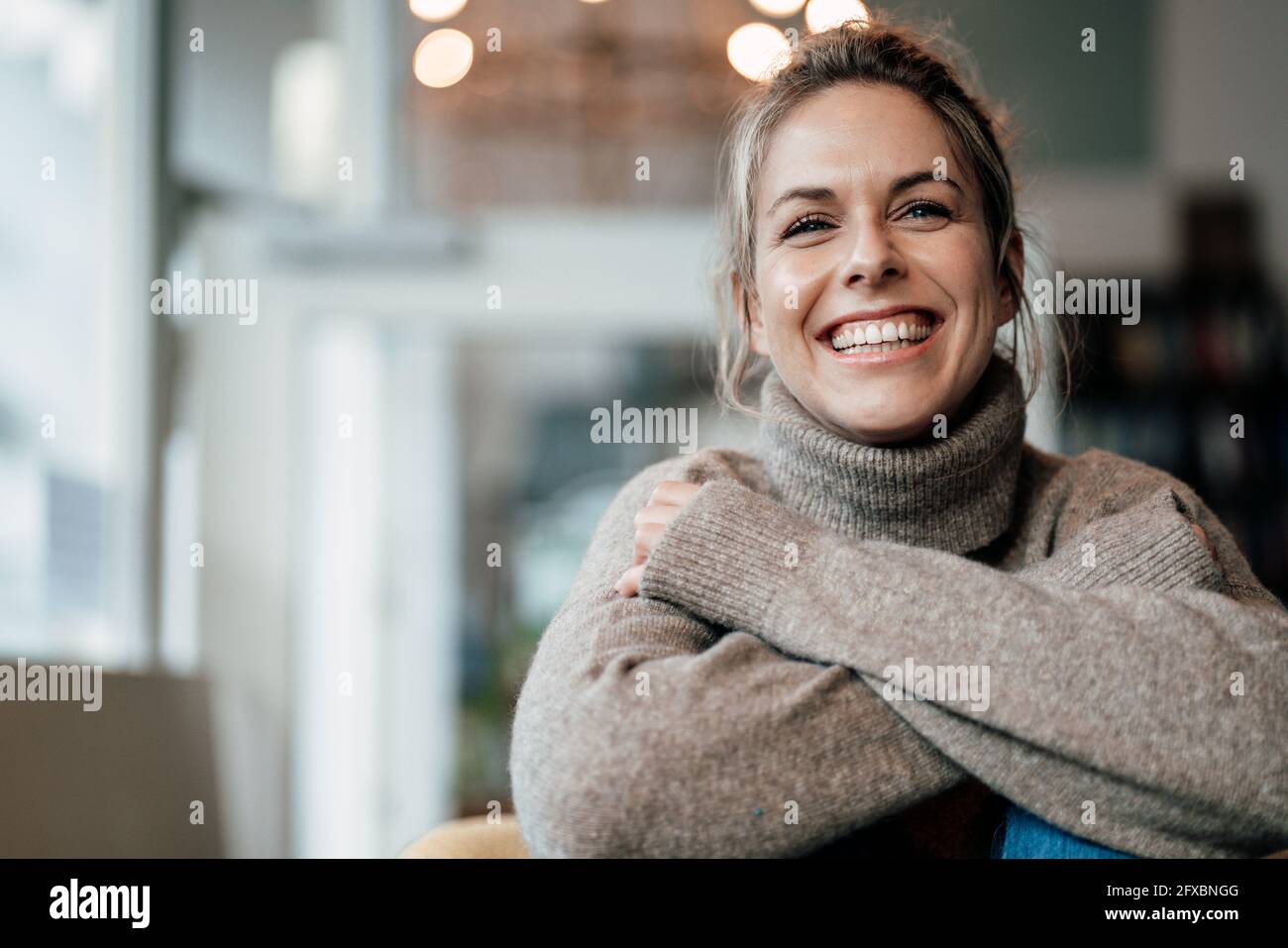 Frau mit mittlerem Erwachsenen, die einen Pullover trägt und im Café lächelt Stockfoto