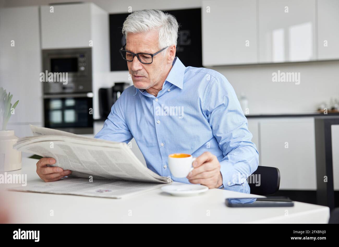 Reifer Geschäftsmann mit Kaffeetasse, die Zeitung in der Cafeteria liest Stockfoto