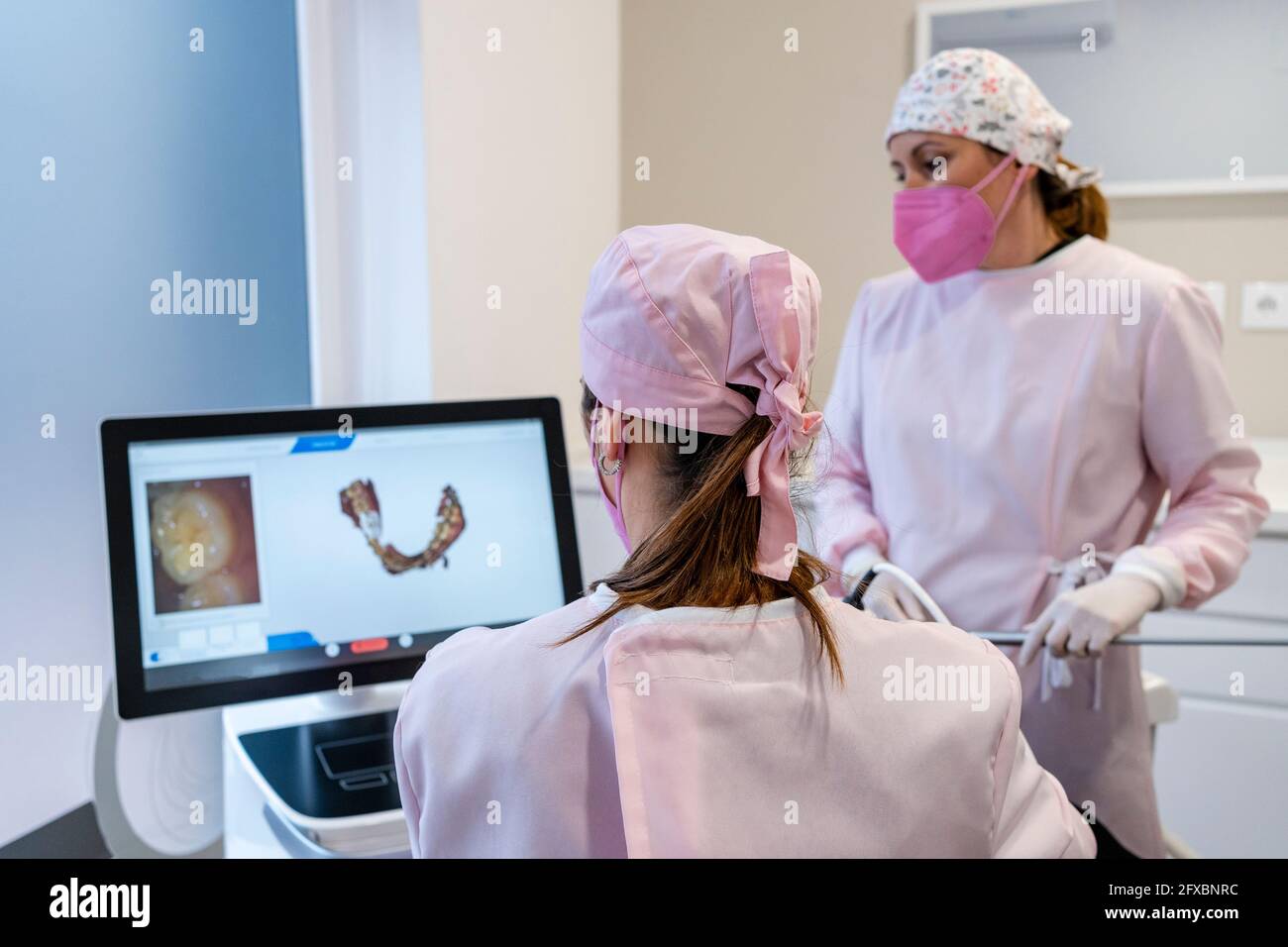 Zahnärztinnen mit chirurgischer Kappe untersuchen digitales Bild der Zähne auf dem Bildschirm in der Klinik Stockfoto