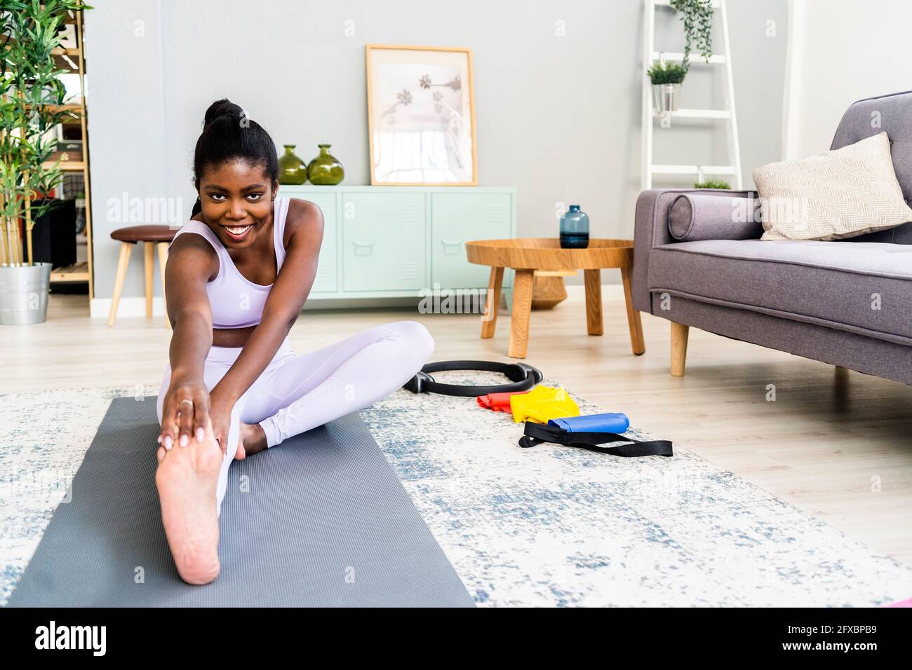 Aktive junge Frau, die sich zu Hause auf einer Yogamatte dehnt Stockfoto