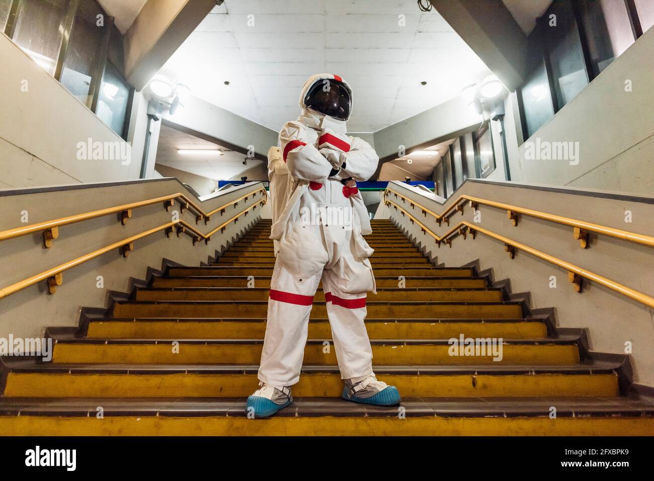 Männlicher Astronaut, der mit gekreuzten Armen auf der Treppe steht Stockfoto