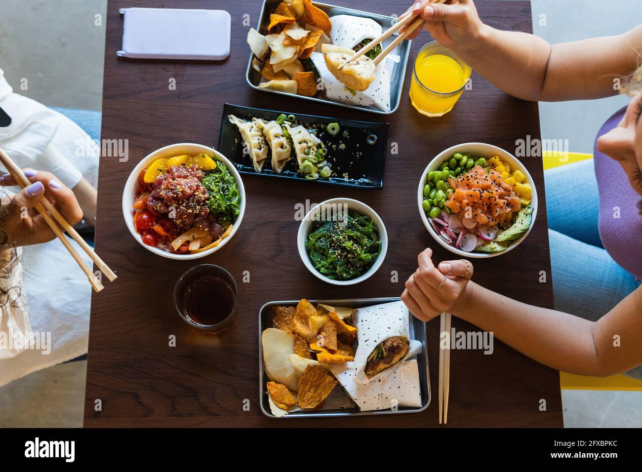 Junge Freundinnen essen mit Essstäbchen auf dem Tisch im Restaurant Stockfoto