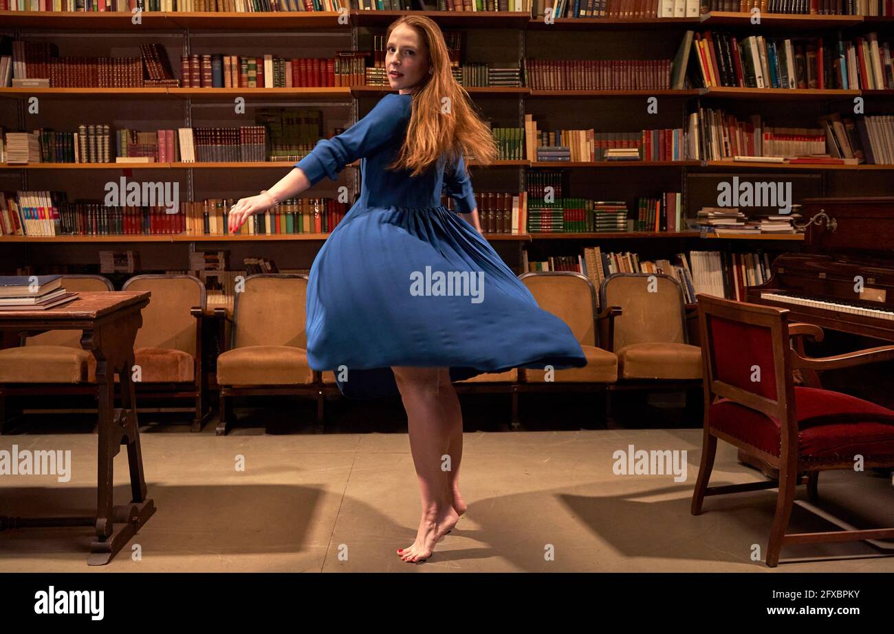 Junge Frau in blauem Kleid tanzt in der Bibliothek Stockfoto