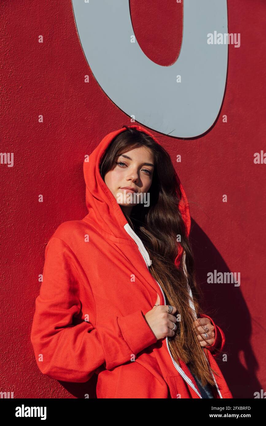 Teenager-Mädchen trägt rote Jacke, während sie sich an die Wand lehnt Stockfoto