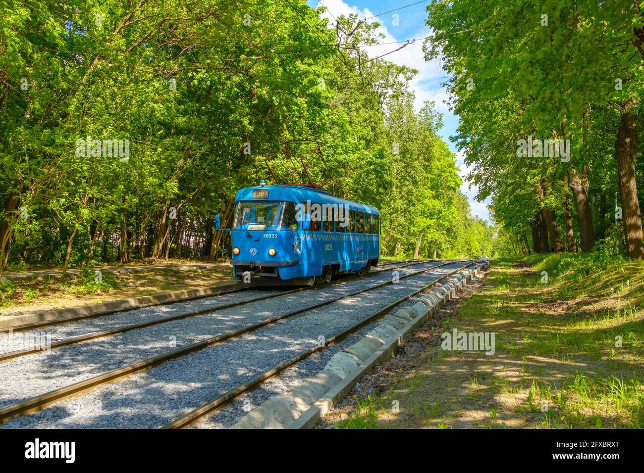 Moskau. Russland. 24.Mai 2021. Die blaue Straßenbahn fährt durch den Stadtpark. Sommersonntag und grünes Laub von Bäumen. Stockfoto