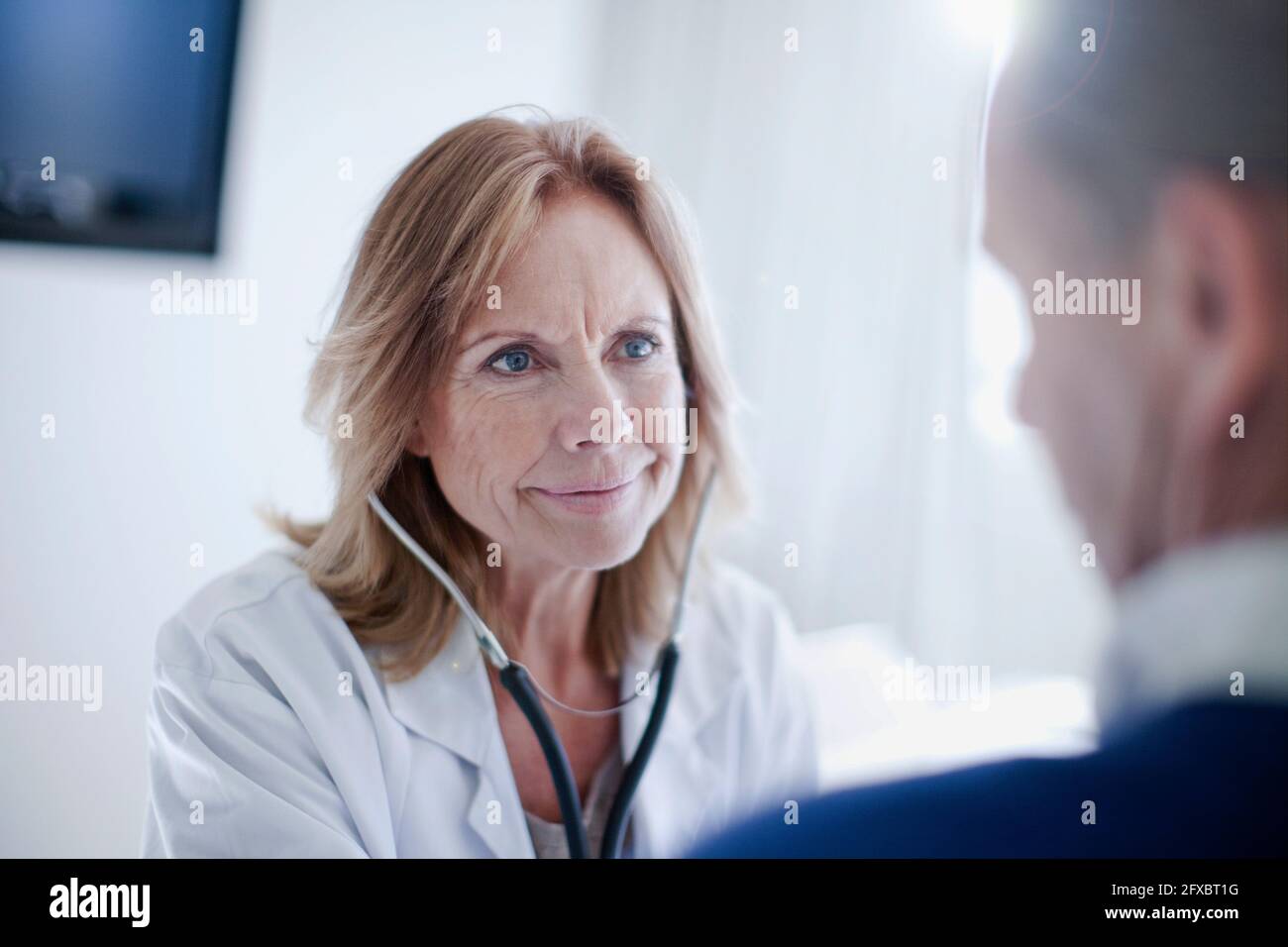 Reifer weiblicher Arzt, der ältere männliche Patienten mit Stethoskop beurteilt Stockfoto