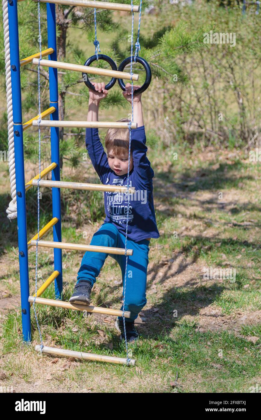 Ein blondes Kind spielt auf dem Spielplatz, hängt an Ringen. Stockfoto