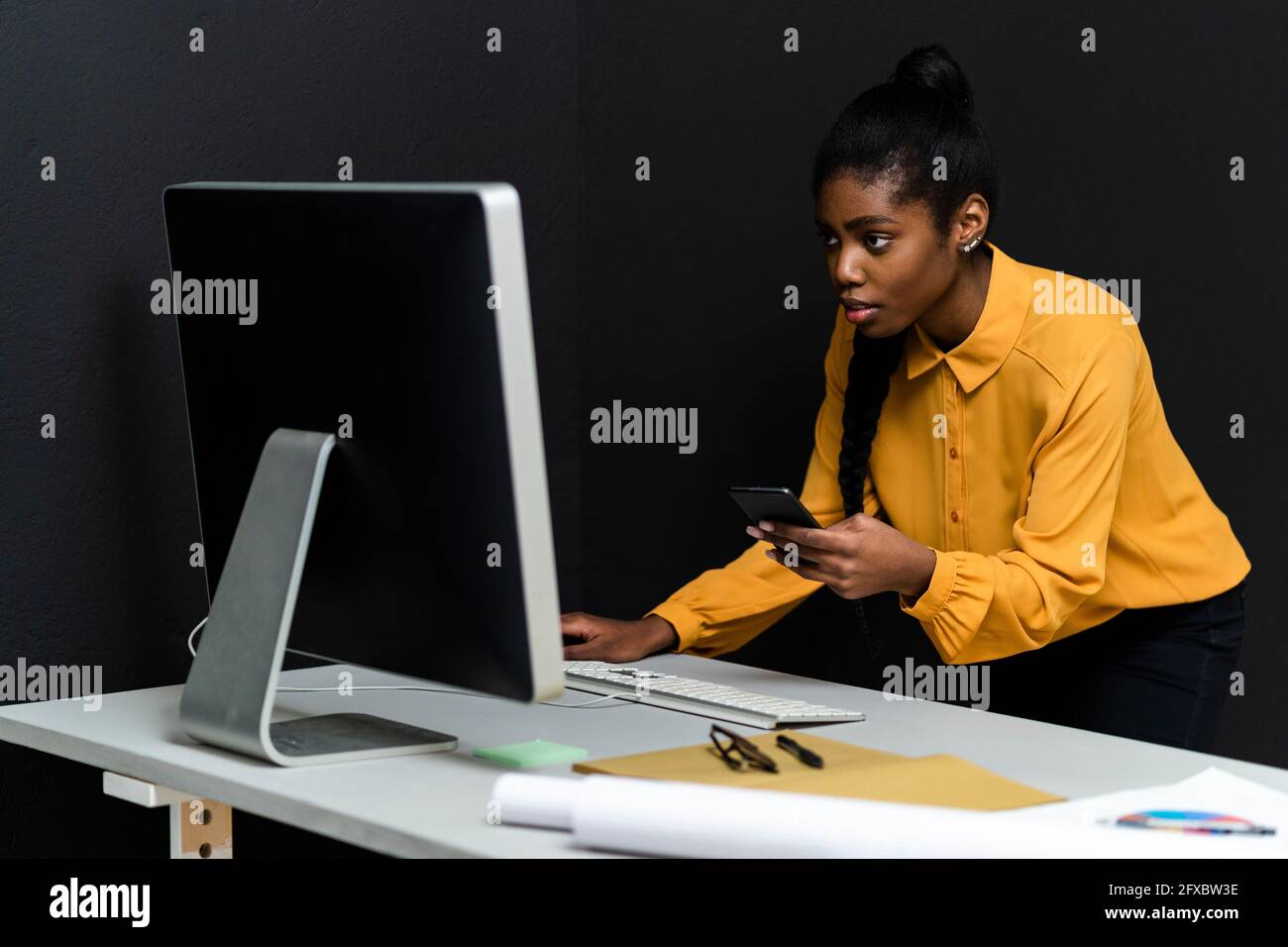 Business-Profi in Smart Casual mit Telefon, während Blick auf den Computer im Studio Stockfoto