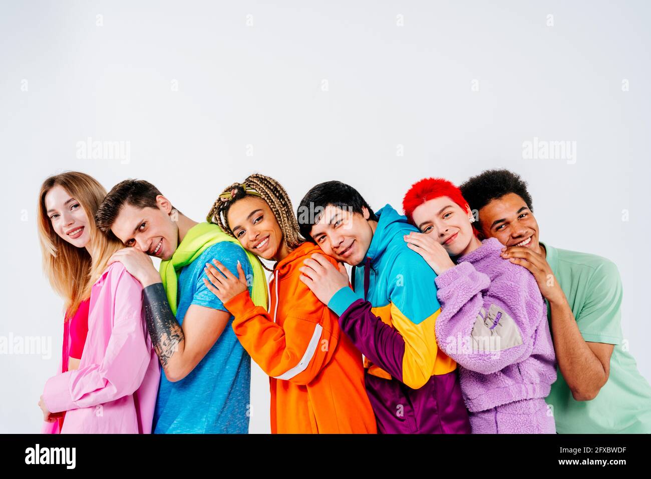 Gruppe von jungen Menschen in bunten Kleidern mit Händen auf der Schulter auf weißem Hintergrund stehen Stockfoto