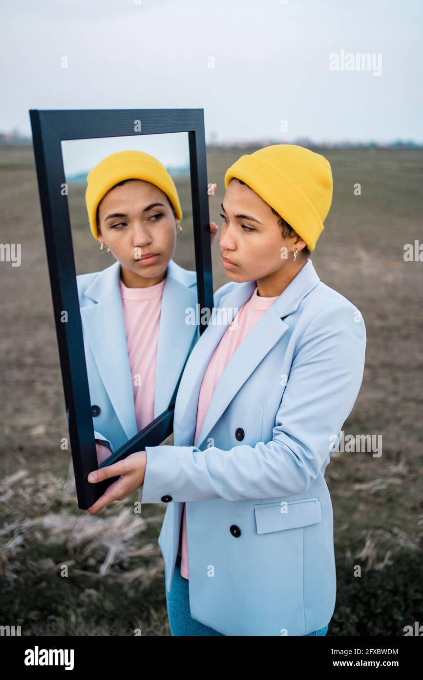 Junge Frau, die die Reflexion im Spiegel auf dem Feld betrachtet Stockfoto