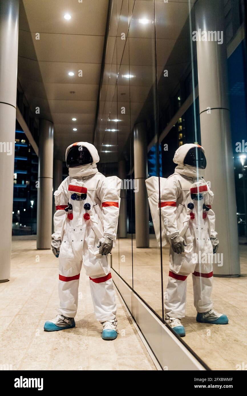Männlicher Astronaut, der nachts an einer Glaswand steht Stockfoto