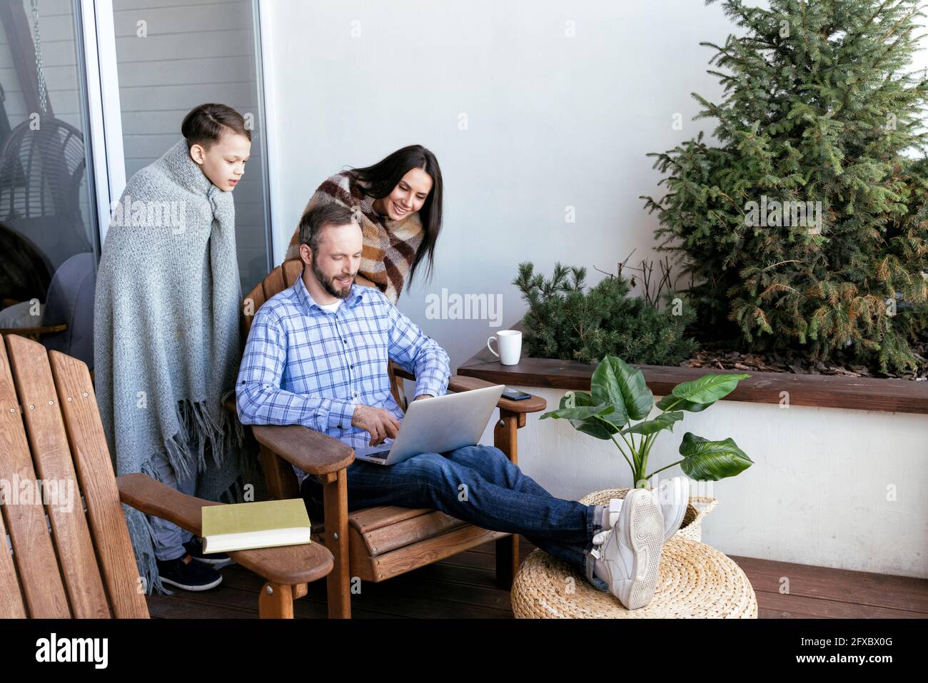 Sohn und Mutter schauen auf den Vater mit dem Laptop auf dem Balkon Stockfoto
