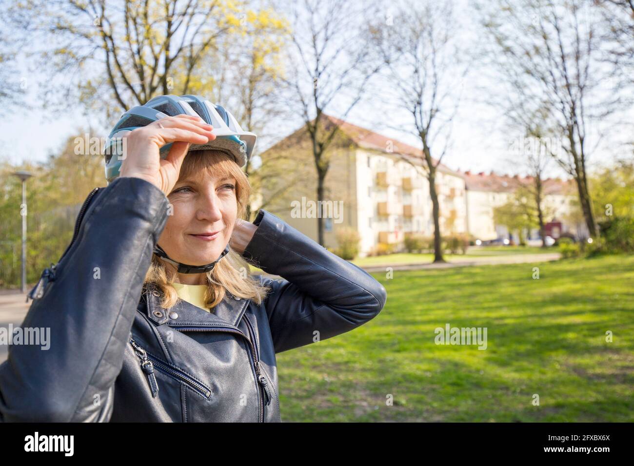 Reife Frau schaut weg, während sie den Helm im Freien anpasst Stockfoto