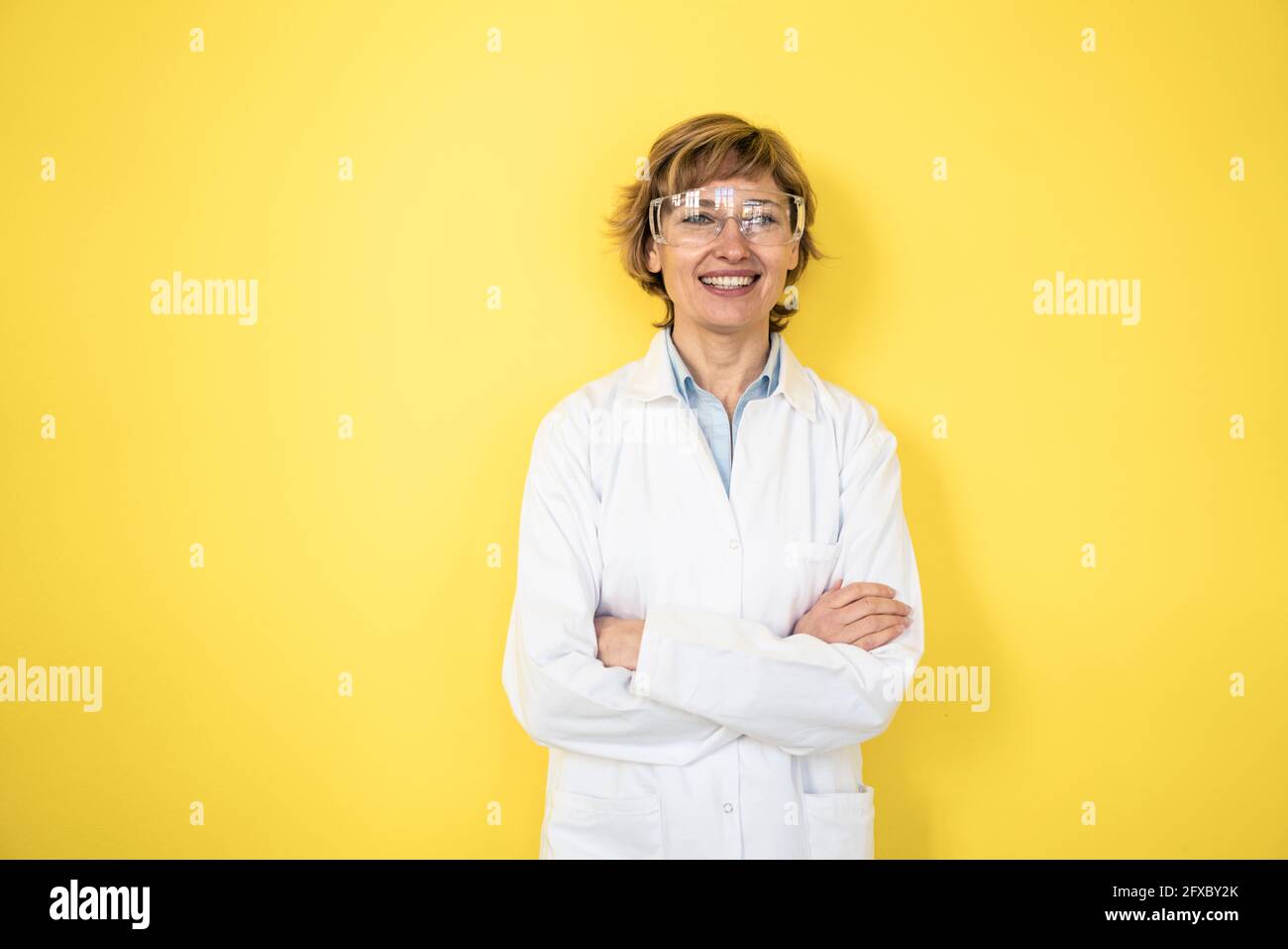 Weibliche Profi trägt schützende Arbeitskleidung, die vor der gelben Wand steht Stockfoto