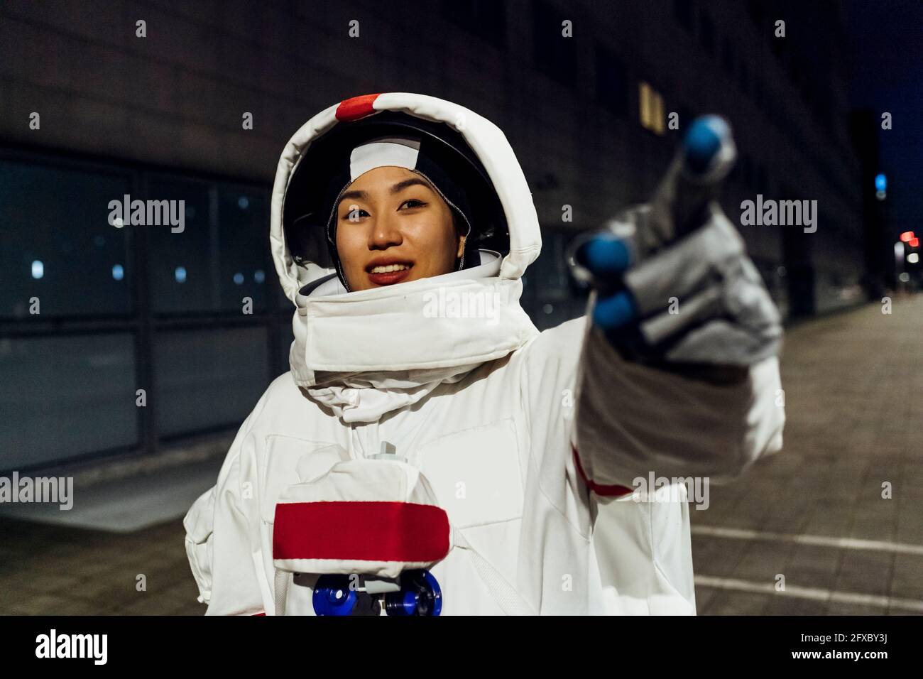 Lächelnde Astronautin im Raumanzug, die nachts auf den Fußweg zeigt Stockfoto