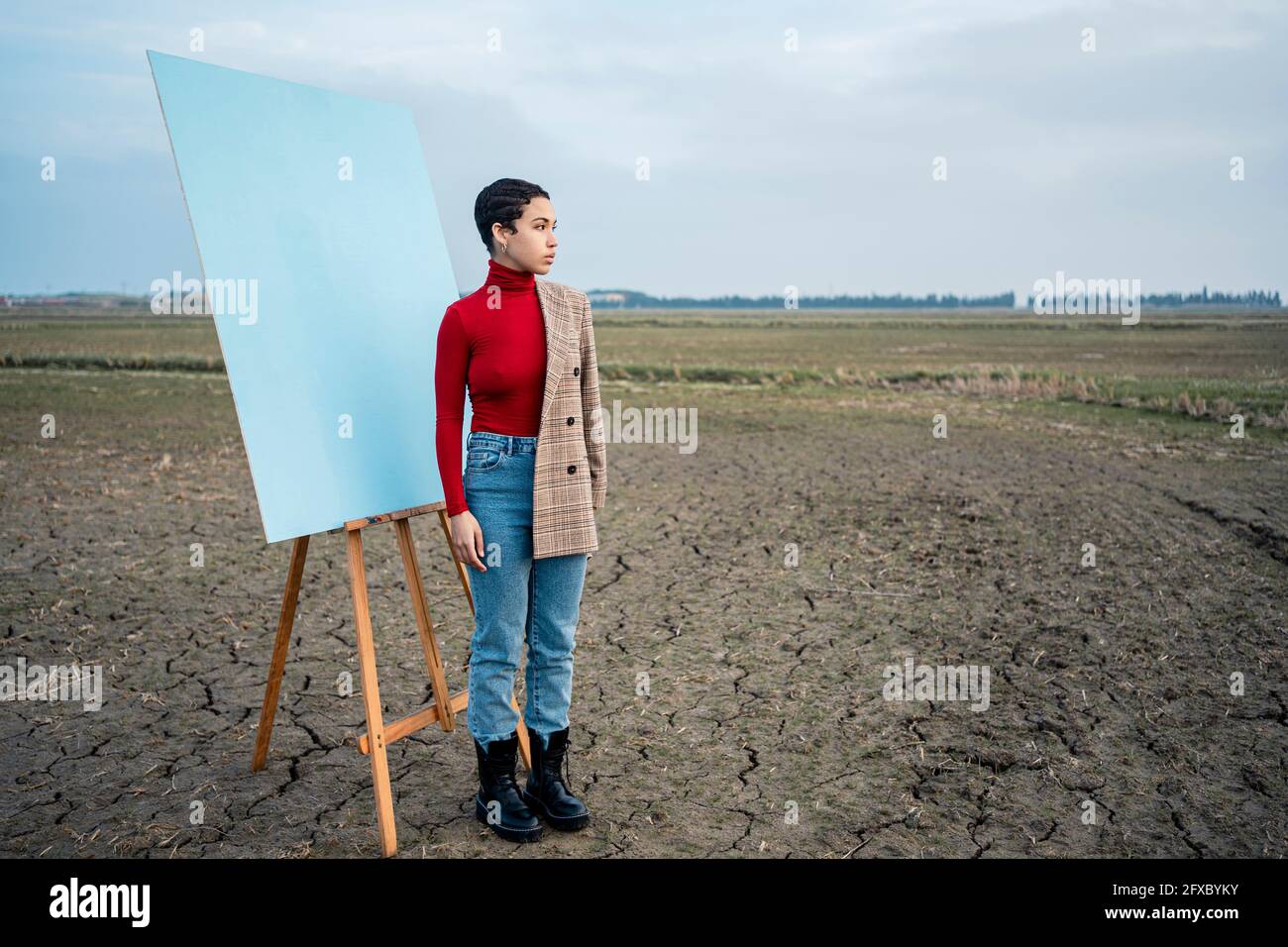 Frau, die beim Malen auf dem landwirtschaftlichen Feld steht und nachdenkt Stockfoto