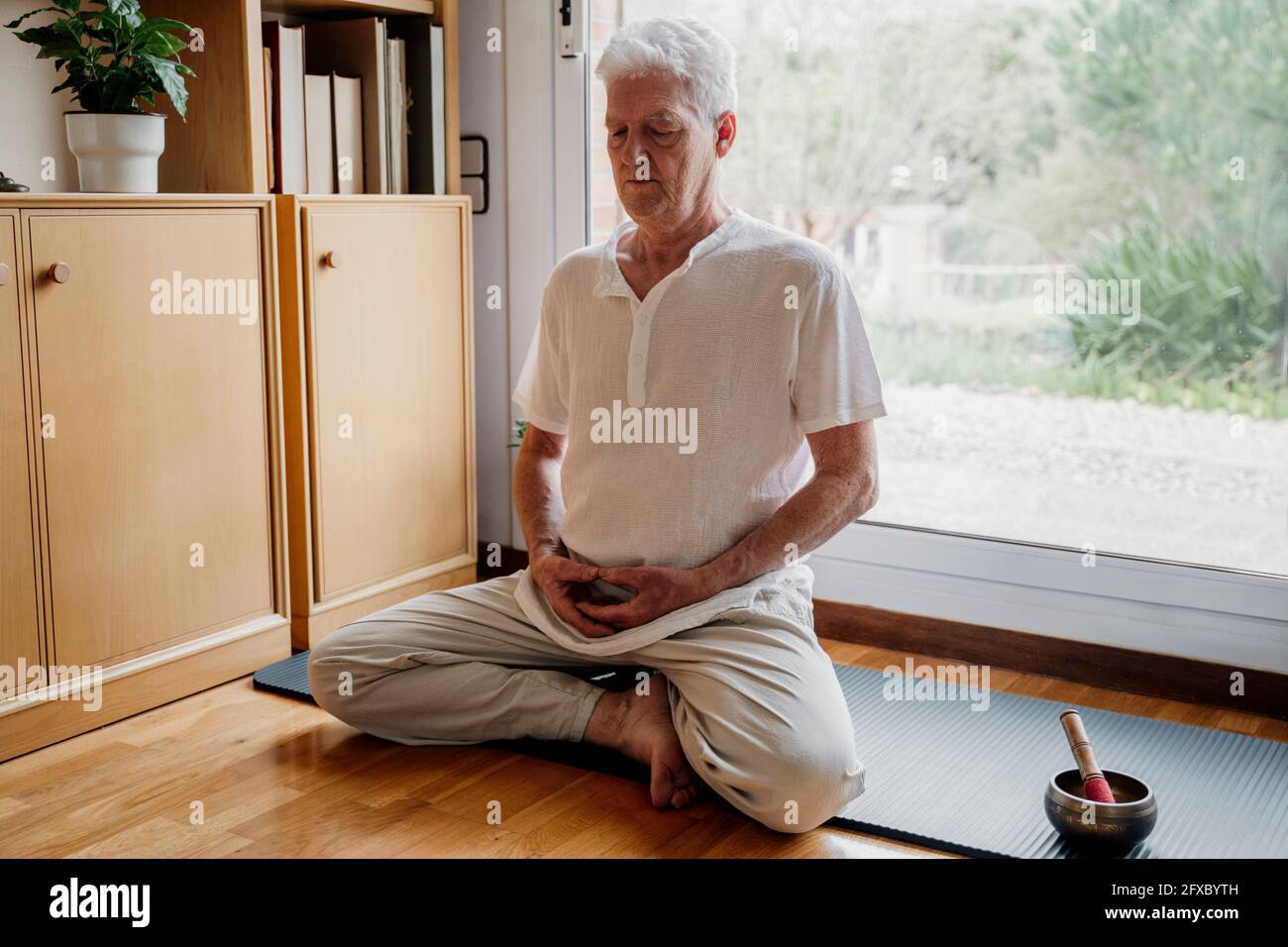Älterer Mann, der zu Hause von der tibetischen Klangschale meditiert Stockfoto