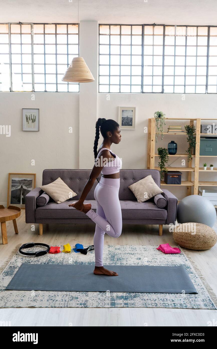 Junge Frau, die auf einem Bein steht, während sie zu Hause trainiert Stockfoto