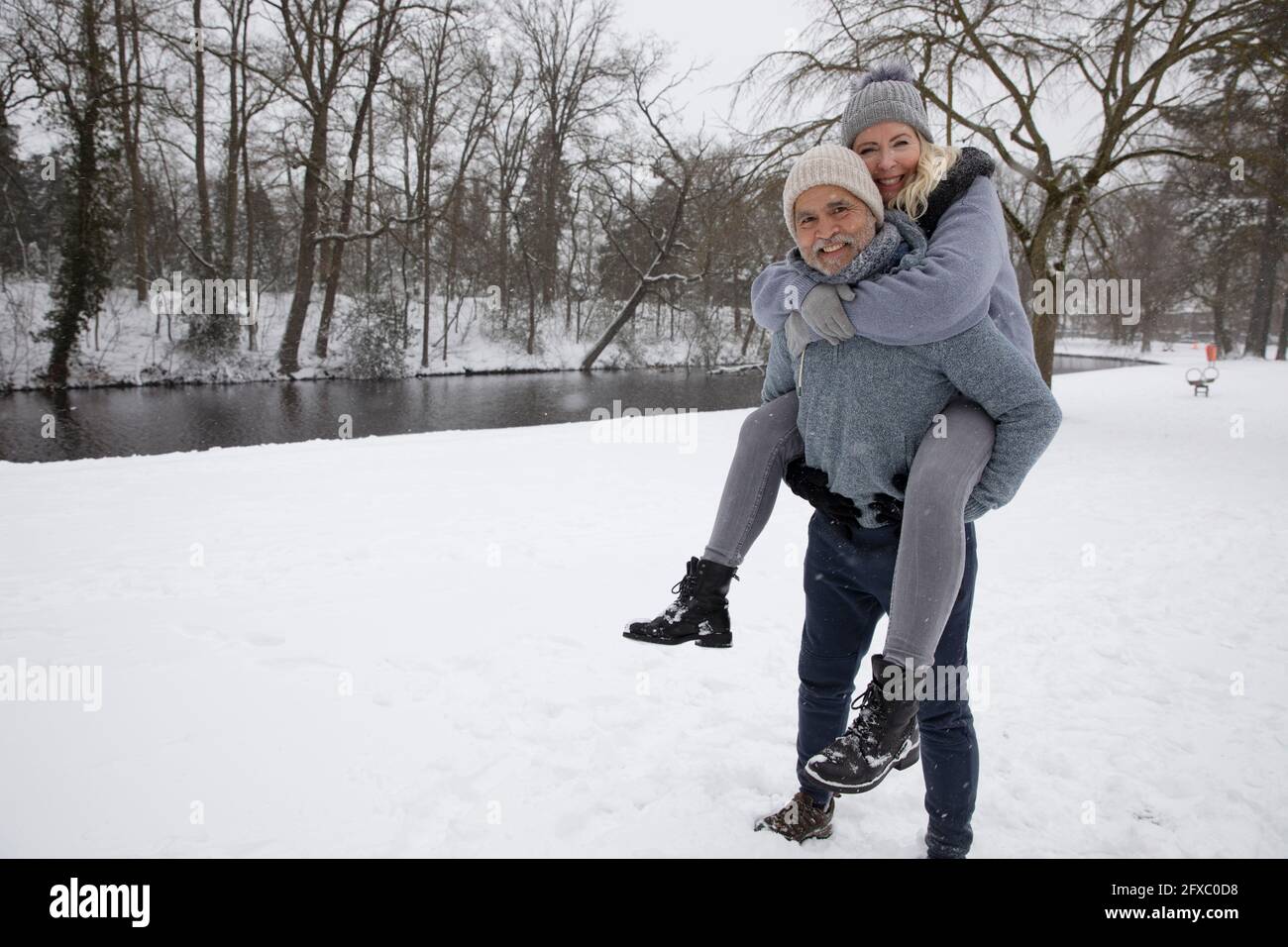 Mann Huckepack verspielte Frau, während auf Schnee stehen Stockfoto