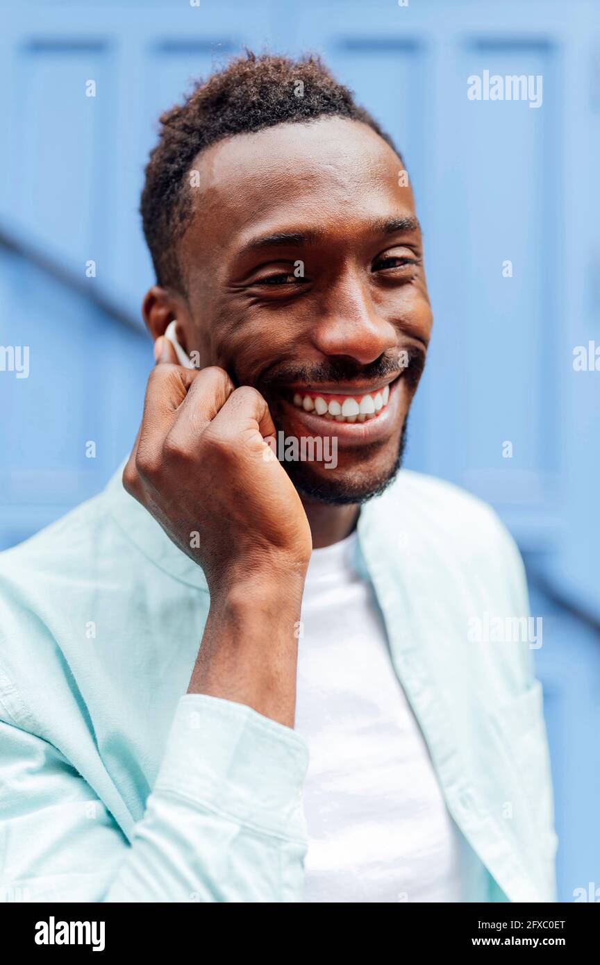 Lächelnder junger Mann in legerer Kleidung mit Ohrhörern Stockfoto