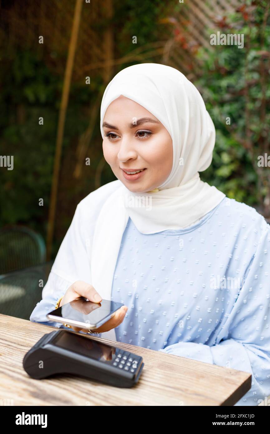 Junge Frau, die im Straßencafé per Smartphone bezahlt Stockfoto