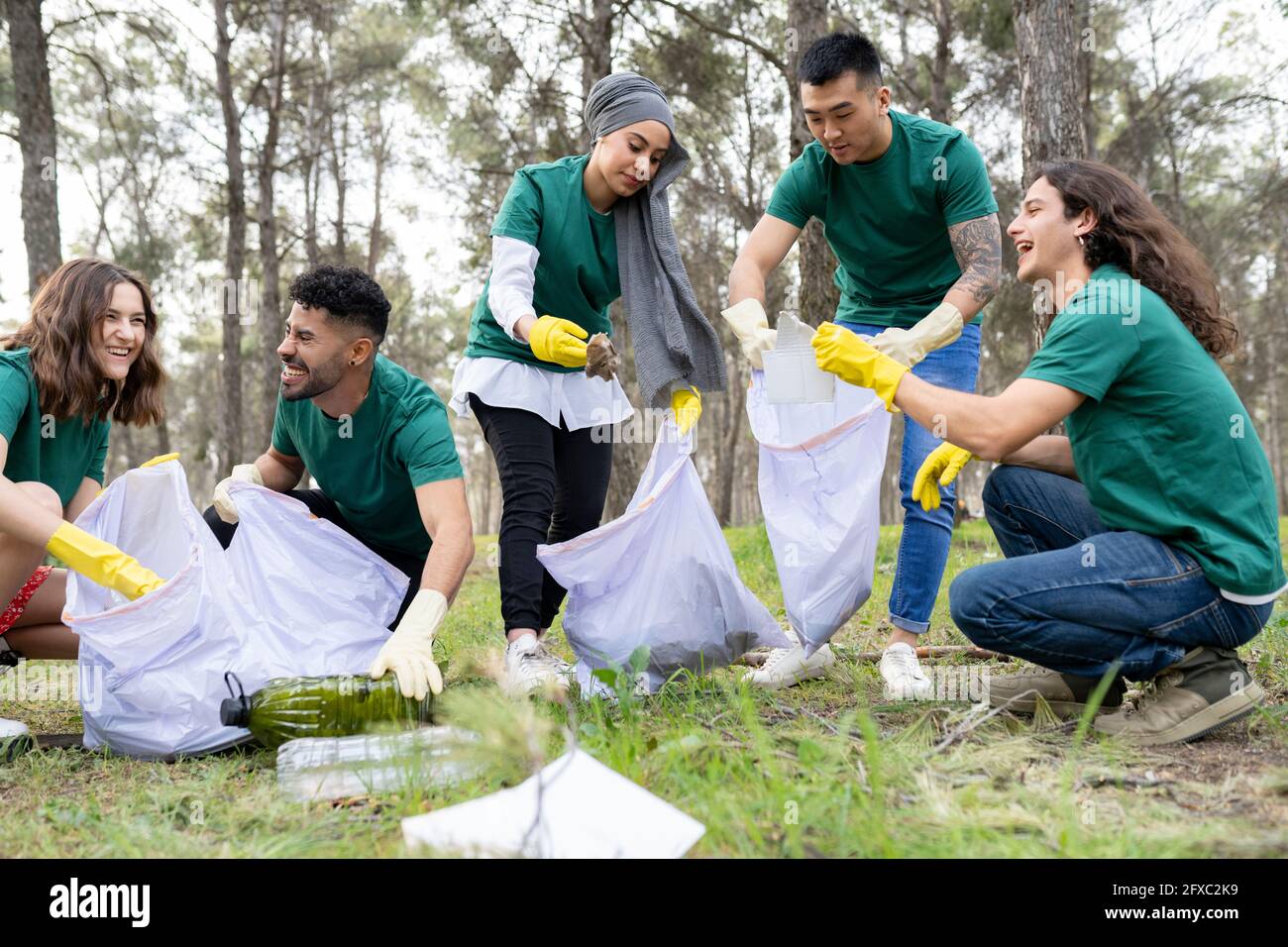 Lächelnde männliche und weibliche Freiwillige sammeln im Wald Plastik Stockfoto