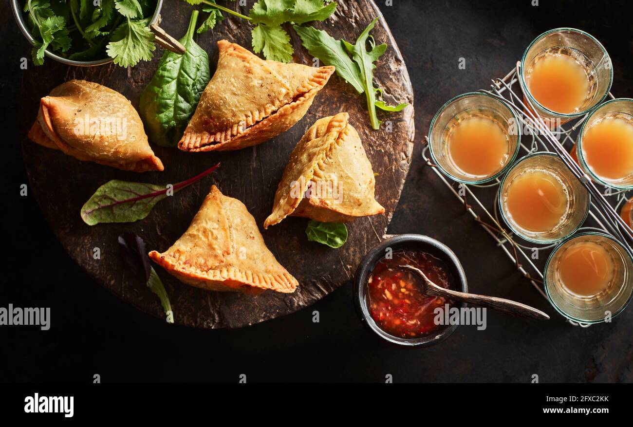 Untersetzer mit Samosa-Knödeln, Rucola-Salat, Schüssel mit Chilisauce und Gläsern Chai-Tee Stockfoto