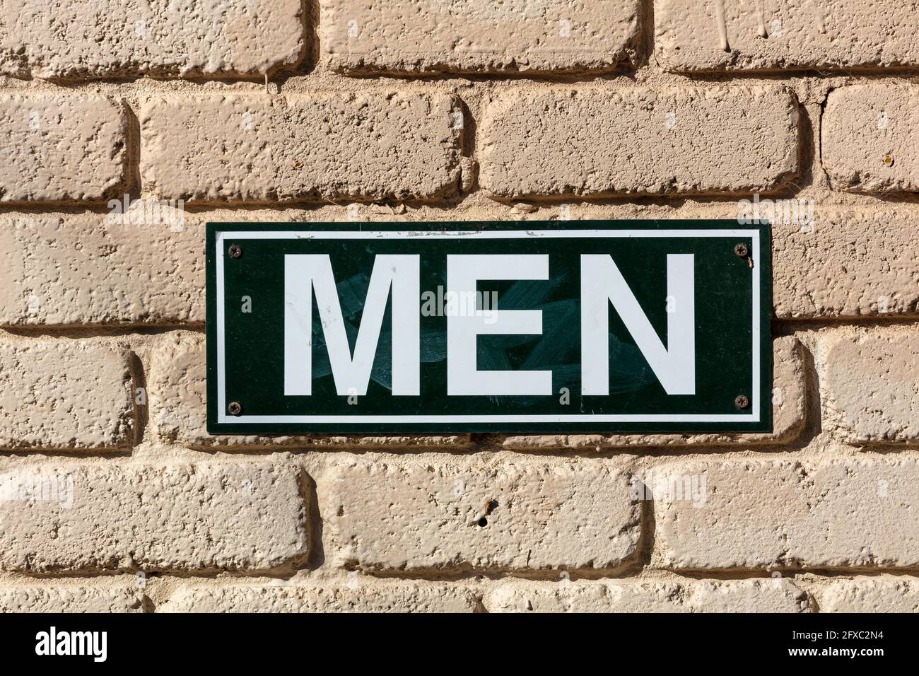 Foto eines schwarz-weiß-metallenen Toilettenschildes für Männer Auf einer hellbraunen Ziegelwand in der Sonne Stockfoto