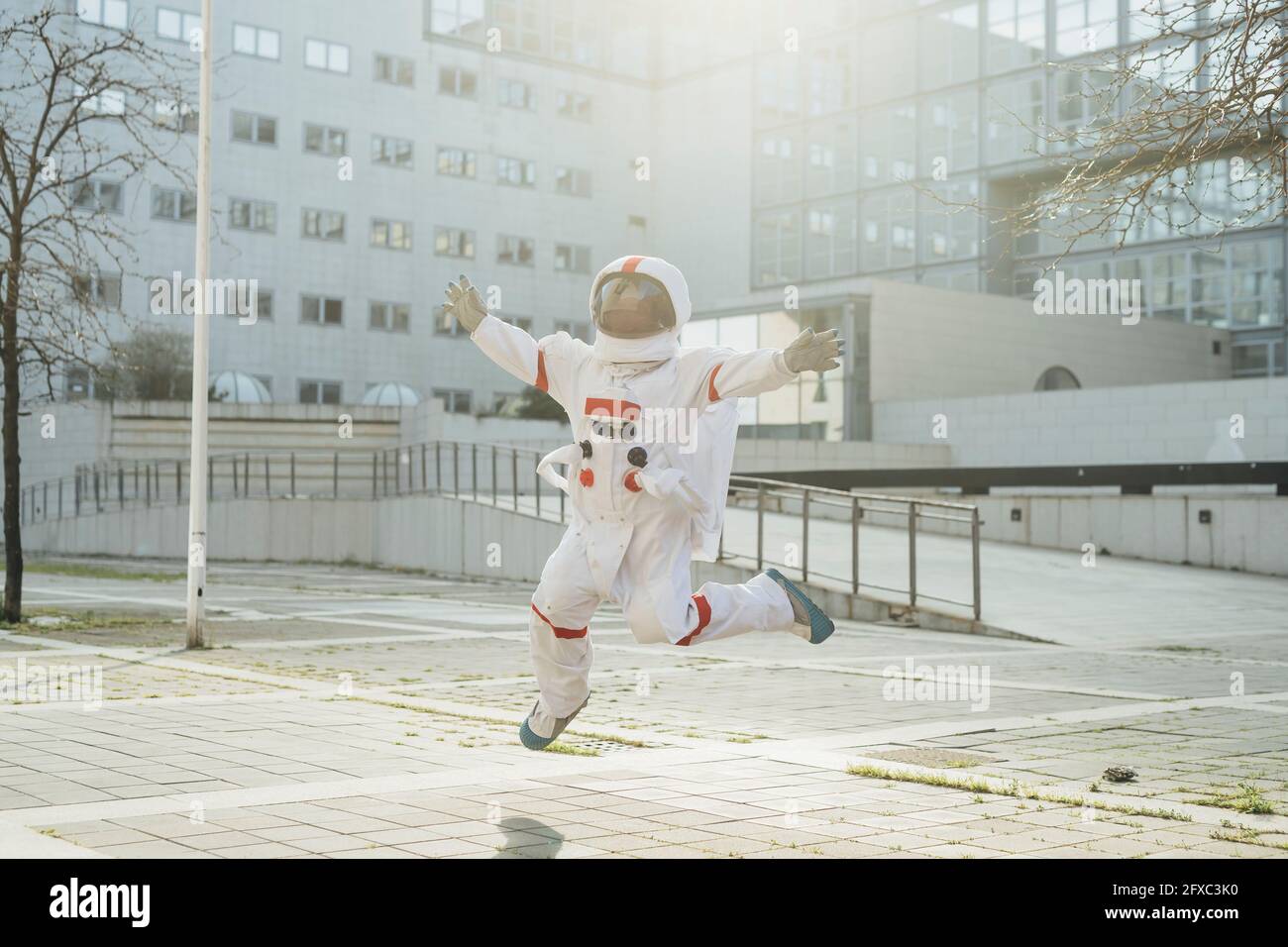 Weibliche Astronautin in der Luft mit ausgestreckten Armen in der Nähe von Gebäuden in der Stadt Stockfoto