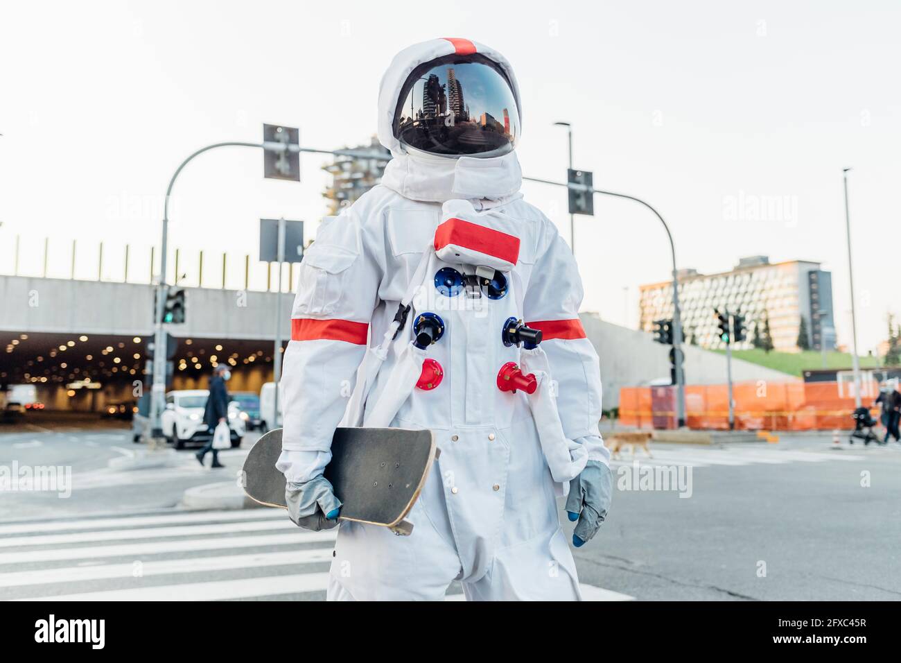 Männlicher Astronaut mit Skateboard auf dem Crosswalk in der Stadt Stockfoto