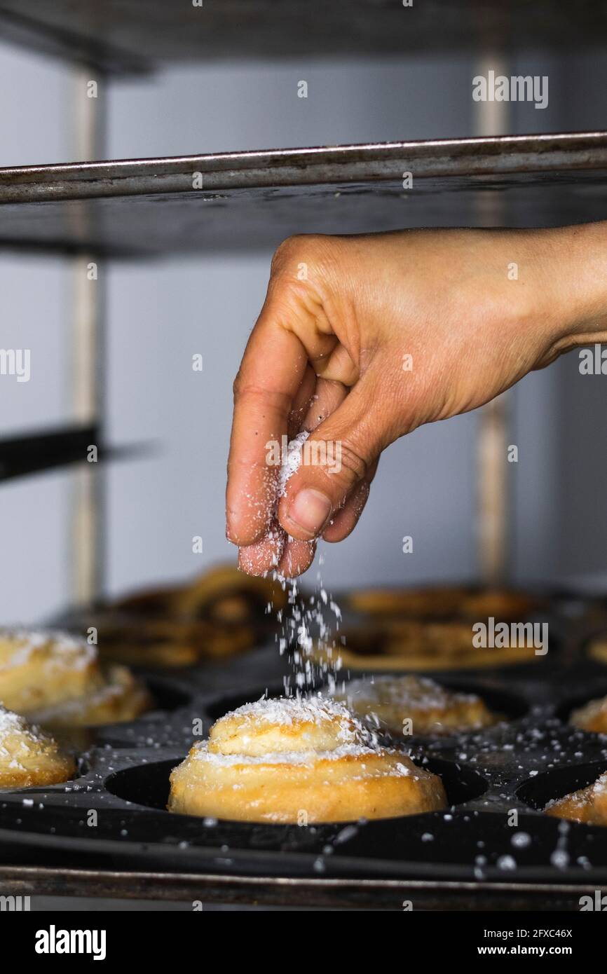 In der Küche Zucker von Hand auf Zimtbrötchen streuen Stockfoto